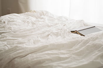 A serene bedroom scene with soft white sheets and a book, evoking relaxation and calm. HD wallpaper