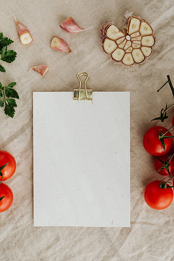 A rustic flat lay featuring a blank clipboard, fresh garlic cloves, and tomatoes, ideal for recipe presentations. HD phone wallpaper