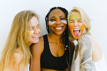 Three diverse women having fun with colorful skincare masks, embodying friendship and joy. HD wallpaper