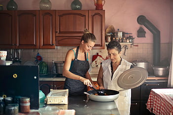 A cheerful mother and daughter cooking a meal together at home, fostering family bonding. HD wallpaper