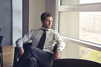 Young businessman in formal attire sitting and looking out of modern office window, contemplating. HD wallpaper