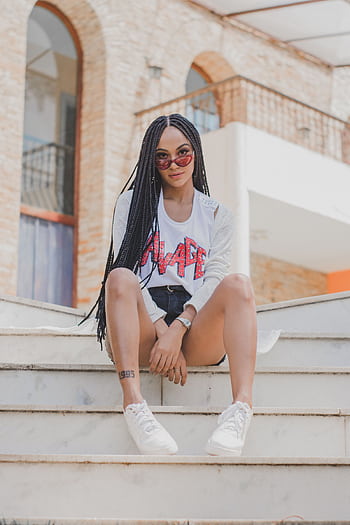 Fashionable young woman posing confidently on urban stairs with sunglasses and braids. HD phone wallpaper