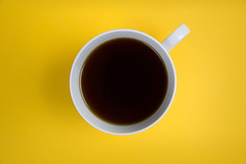A simple and bold composition featuring a black coffee cup on a vibrant yellow background. Perfect for modern designs. HD wallpaper