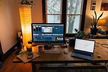 A cozy home office setup featuring a laptop, monitor, and warm lighting, perfect for remote work. HD wallpaper