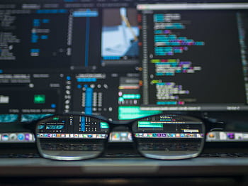 Eyeglasses reflecting computer code on a monitor, ideal for technology and programming themes. HD wallpaper