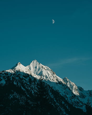 Stunning view of snow-capped mountain peaks with a crescent moon in the clear blue sky at dusk. HD phone wallpaper