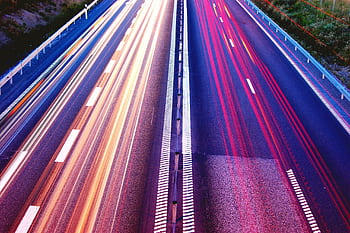 Long exposure capture of vibrant light trails on a highway at dusk, showcasing motion and speed. HD wallpaper