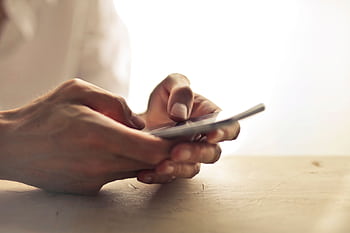 Close-up of an individual's hands holding a smart on a table indoors. HD wallpaper