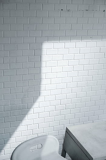 A minimalist white brick wall casting a shadow, paired with a modern chair and table. HD phone wallpaper