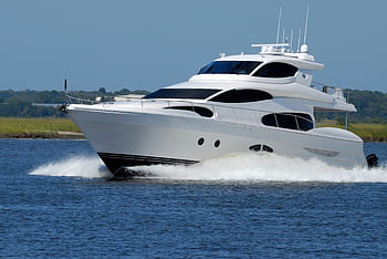 A modern luxury yacht cruising swiftly on a calm river under a clear blue sky. HD wallpaper