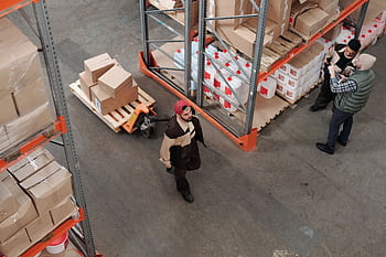 Team working in an industrial warehouse discussing and organizing inventory with pallets. HD wallpaper