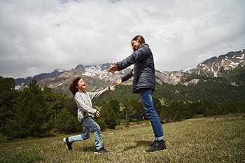 A mother and child embrace joyfully in a lush mountain setting, capturing a moment of happiness and love. HD wallpaper