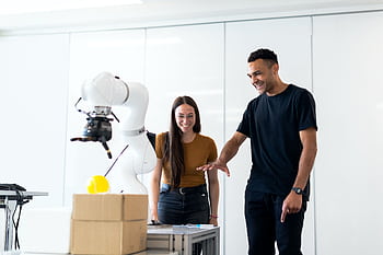 Two engineers collaborating on testing a futuristic robotic prototype in a modern indoor lab. HD wallpaper