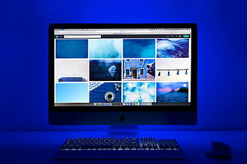 Modern workspace with a glowing blue theme and a computer monitor showcasing a gallery of . HD wallpaper