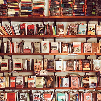 A vibrant collection of books neatly arranged on wooden shelves in a cozy library setting. HD phone wallpaper