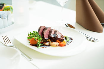 A beautifully presented beef steak with vegetables and sauce in a fine dining setting. HD wallpaper
