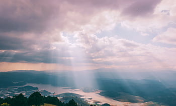 Gentle sunbeams breaking through a cloudy sky over a serene landscape. HD wallpaper