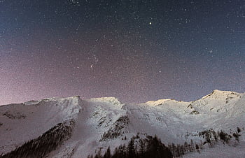 A breathtaking view of snow-capped mountains under a starry night sky, capturing the beauty of winter outdoors. HD wallpaper