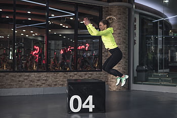 Fit young woman in sports wear executing a box jump indoors, promoting fitness and health in a modern urban gym. HD wallpaper