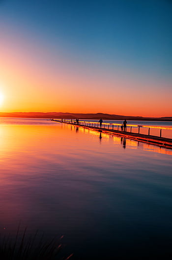 A breathtaking sunset view over a tranquil boardwalk and waterway, reflecting vibrant colors. HD phone wallpaper