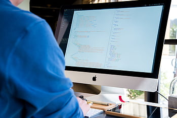 A programmer in a blue shirt coding on an iMac. Perfect for technology or work-related themes. HD wallpaper
