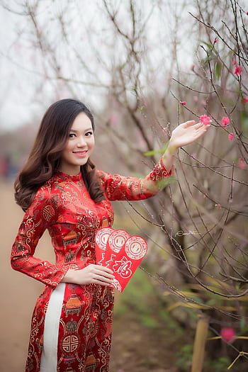 Young woman in traditional Vietnamese dress holding red envelopes in a blossoming garden. HD phone wallpaper
