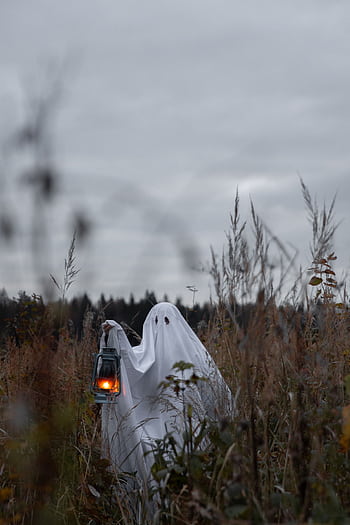 Eerie ghostly figure holding a lantern in a misty field, perfect for Halloween themes. HD phone wallpaper