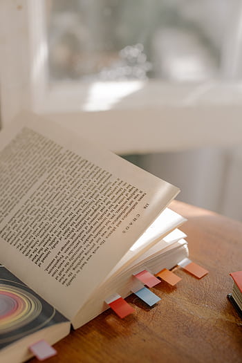 Open book with vibrant bookmarks, basking in warm natural light. HD phone wallpaper