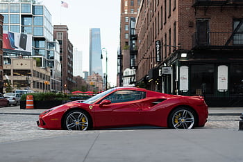 A luxurious red Ferrari sports car parked in urban New York City against a backdrop of modern and vintage buildings. HD wallpaper