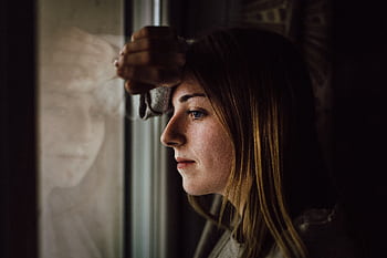 A contemplative young woman looks out a window with a reflective expression, indoors. HD wallpaper