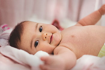 Cute baby lying on a soft bed, expressing innocence and joy in a cozy indoor setting. HD wallpaper