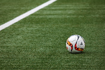 A vibrant soccer ball resting on a pristine grass field beside a white sideline. HD wallpaper