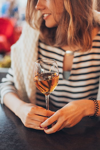 A woman with striped shirt holding a wine glass indoors, creating a warm and fashionable ambiance. HD phone wallpaper
