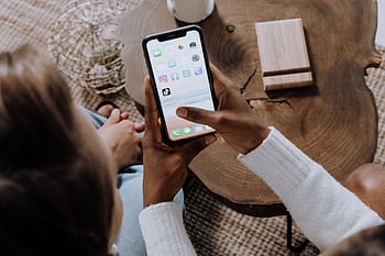 A person using a smart with social media apps, sitting at a wooden table. Perfect for tech lifestyle content. HD wallpaper