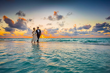 A young couple enjoying a romantic beach wedding during a vibrant sunset. HD wallpaper