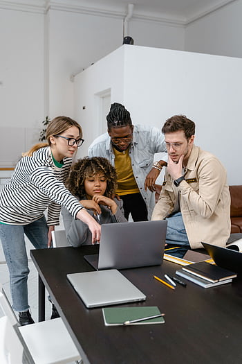 Diverse group of coworkers collaborating on a project using a laptop in a modern office. HD phone wallpaper
