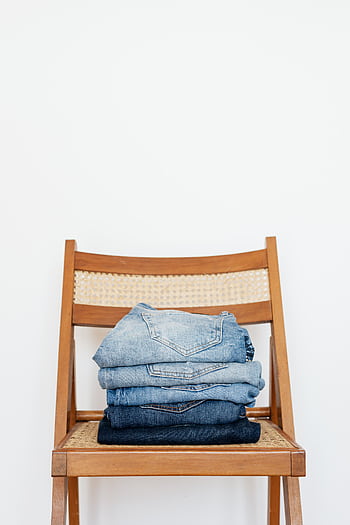 A neat stack of folded denim jeans placed on a minimalist wooden chair indoors. HD phone wallpaper