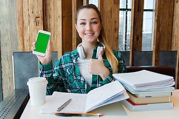 Smiling young woman using a smart while studying with books, showcasing modern education. HD wallpaper