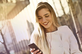 Happy woman listening to music on her smart with ears while walking outdoors. HD wallpaper