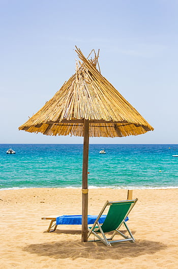 Serene beach scene in Sardinia, Italy featuring a sunshade and lounge chairs by turquoise waters. HD phone wallpaper