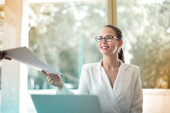 Smiling businesswoman in a modern office handing over documents, symbolizing professionalism and teamwork. HD wallpaper