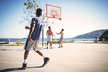 People playing basketball on an outdoor court with a scenic view at Avila Beach. HD wallpaper