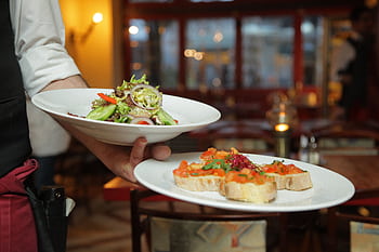 A waiter serves a fresh salad and hors d'oeuvres in a cozy restaurant setting. HD wallpaper