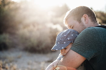 A father lovingly embraces his baby outdoors on a sunny day. Perfect for Father's Day themes. HD wallpaper