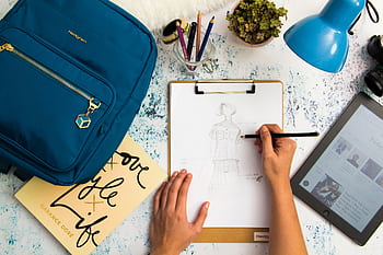 Top view of a designer sketching fashion ideas in a creative workspace with various tools. HD wallpaper