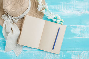 A creative flat lay featuring a straw hat, a blank notebook, and a pencil on a blue wooden surface. HD wallpaper