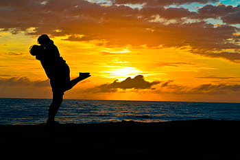Silhouette of a romantic couple embracing on a beach at sunset, showcasing love and tranquility. HD wallpaper