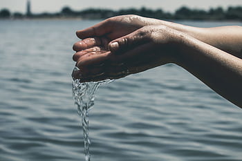 A pair of hands cupping water from a serene lake, symbolizing purity and conservation. HD wallpaper