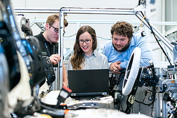 Engineers collaborating on a car project in a modern automotive workshop using advanced technology. HD wallpaper