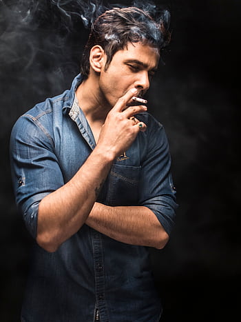Portrait of a fashionable man smoking a cigarette in a moody, dark setting wearing denim. HD phone wallpaper